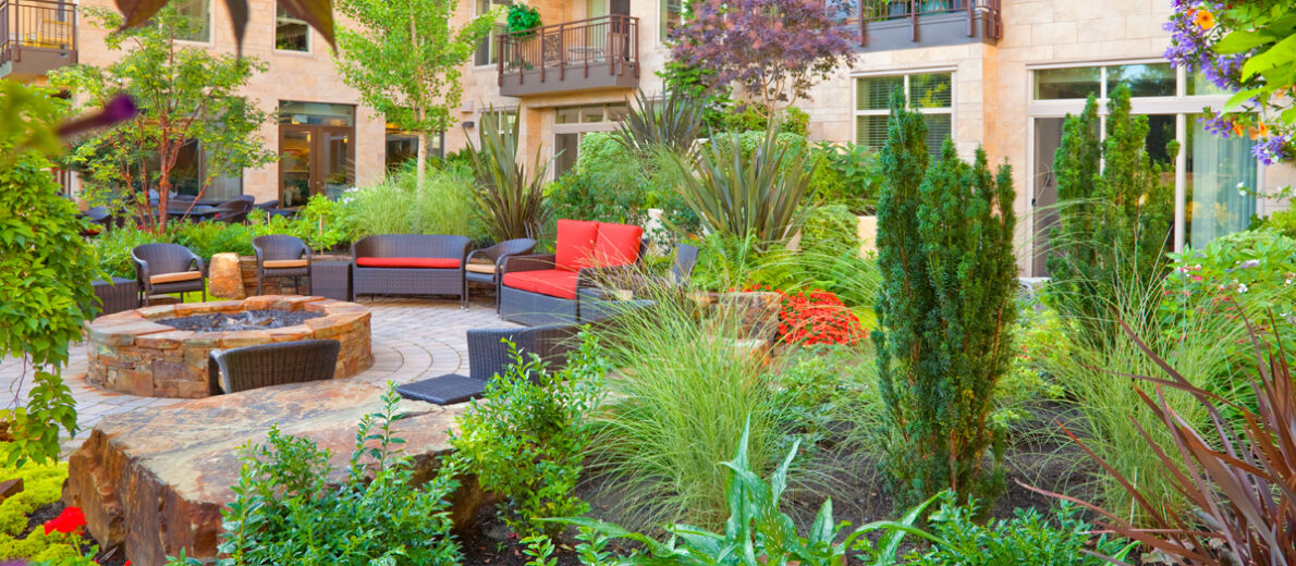 Inviting courtyard garden at the Aljoya Mercer Island retirement community, featuring lush landscaping, comfortable seating, water feature, and fire pit for seniors to relax and socialize outdoors in Mercer Island.