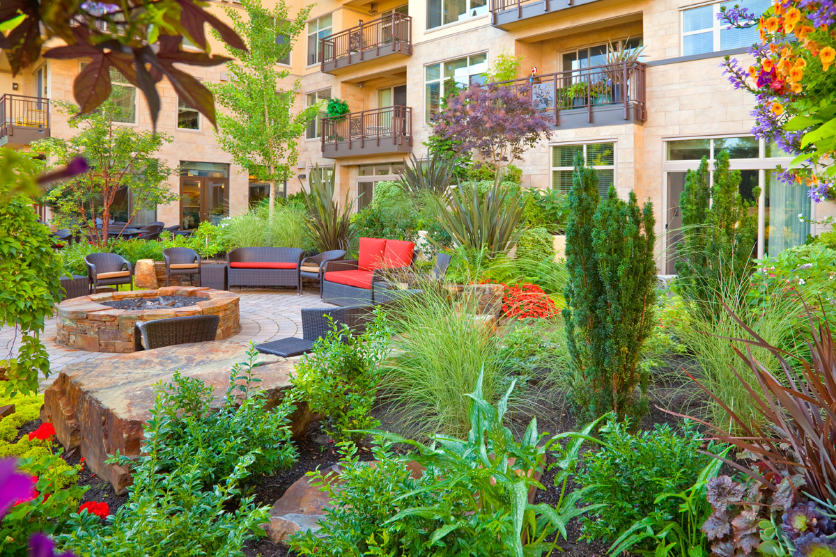 Inviting courtyard garden at the Aljoya Mercer Island retirement community, featuring lush landscaping, comfortable seating, water feature, and fire pit for seniors to relax and socialize outdoors in Mercer Island.