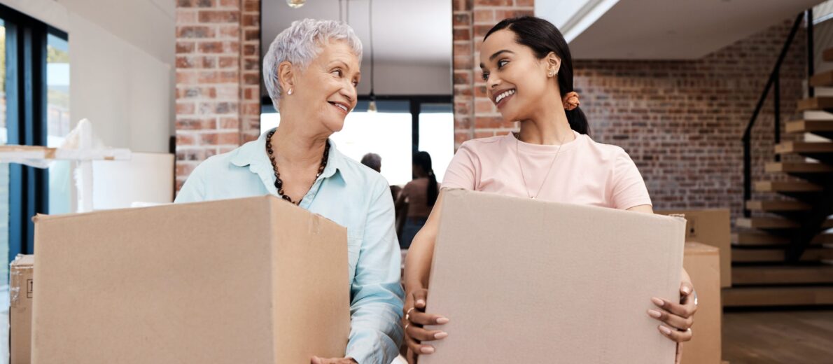 Grandma and her granddaughter in a living room holding moving boxes and working on downsizing
