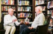 two gentlemen talking in the library while sipping whiskey