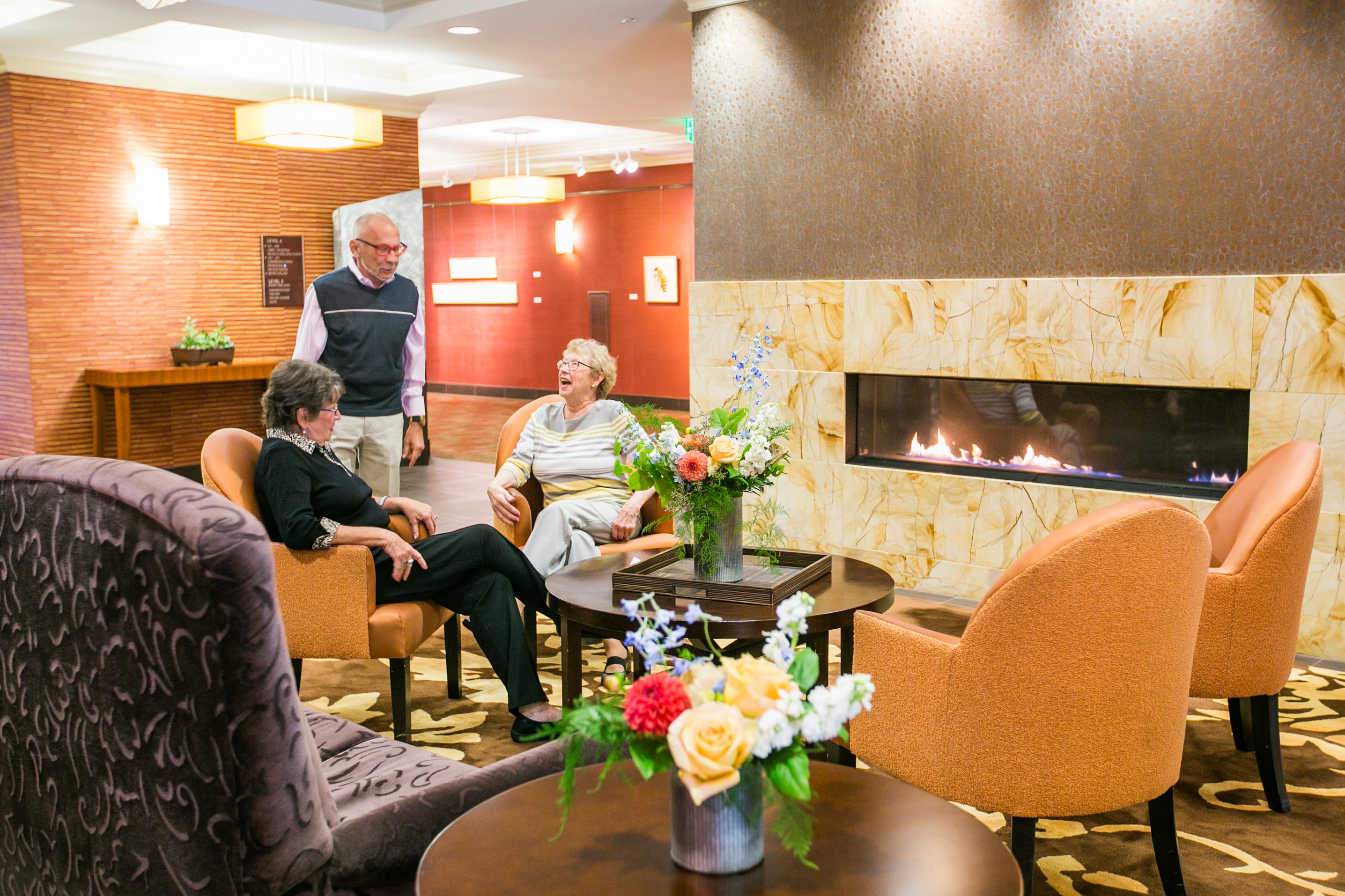 Older adults enjoying community and warmth by the fireplace in the lobby of the Aljoya Thornton Place retirement community in Seattle.