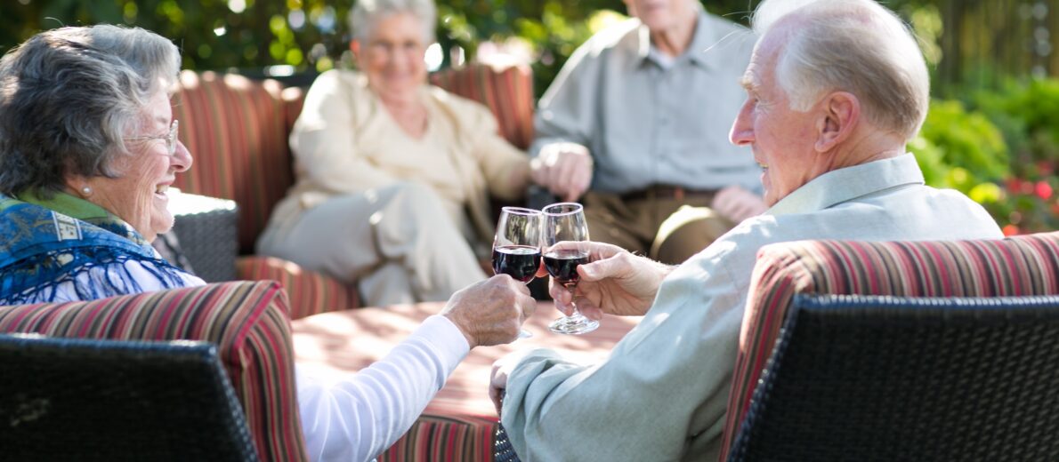 Older couple enjoying time outside in the garden with friends drinking wine.