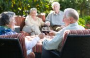 Older couple enjoying time outside in the garden with friends drinking wine.