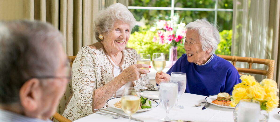 three older adults dining together and cheering at University House Issaquah senior living retirement community.