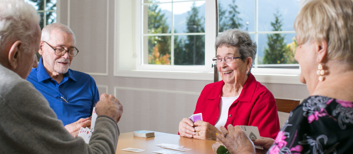 Friends laughing and playing cards with a view of the mountains out the window.