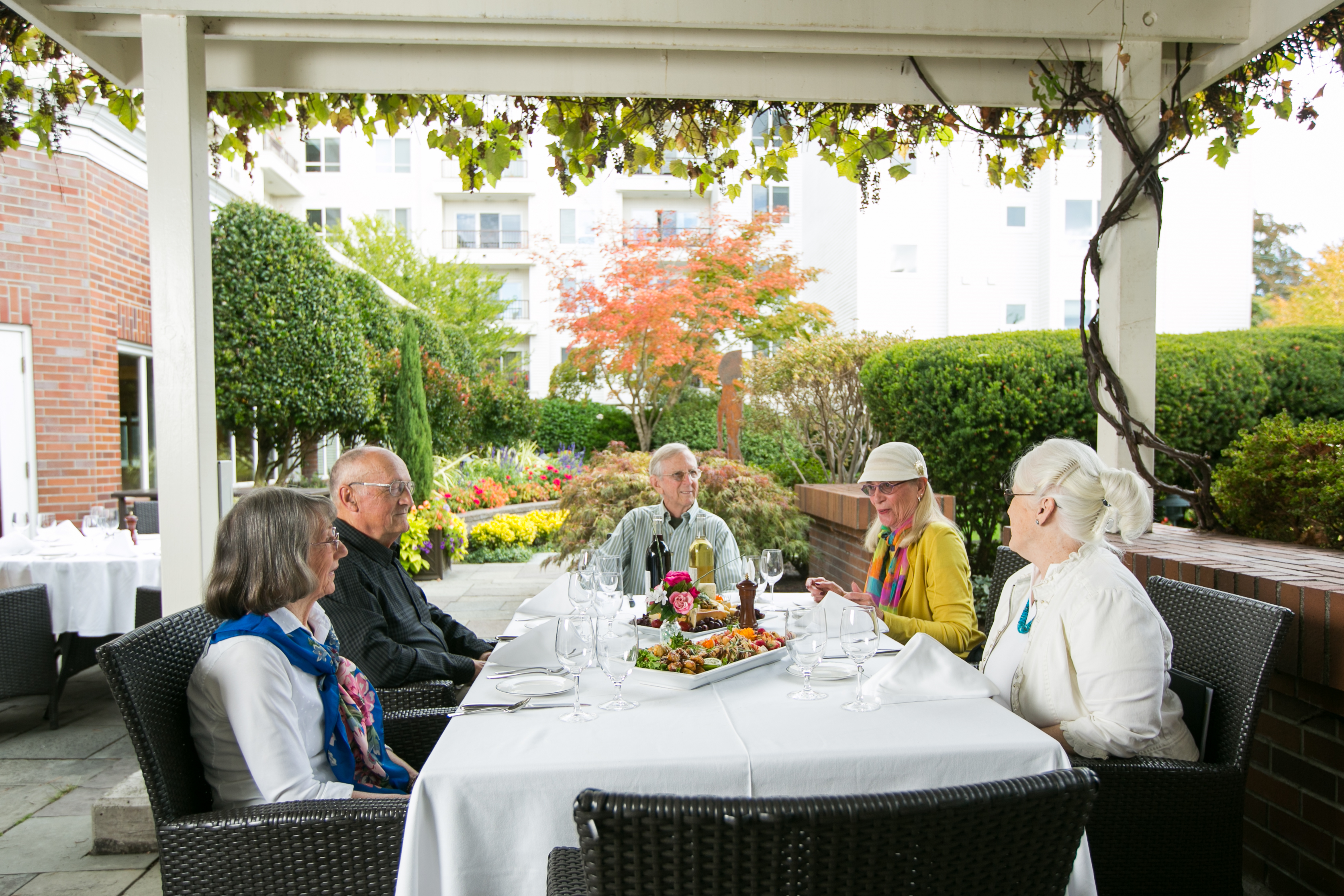 Friendly neighbors in a group setting enjoying lunch outside in courtyard of Seattle retirement community