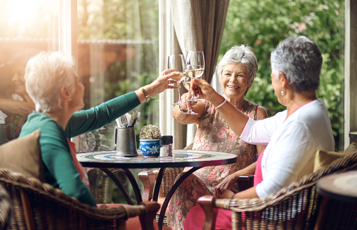 3 happy elder women sitting at a table toasting with a glass of champagne.