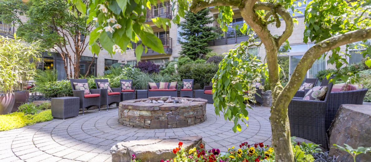 Serene outdoor garden courtyard at the Aljoya Mercer Island retirement community in Mercer Island, featuring a fire pit, comfortable seating, and lush greenery for relaxation.
