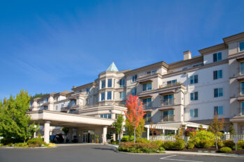 Entrance to University House Issaquah with a clear blue sky and lush landscaping