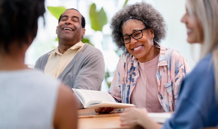 A group of smiling people sitting together reading poetry.