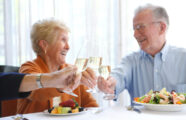 An older couple toasting with champagne and enjoying a healthy meal together at the Aljoya Mercer Island retirement community in Mercer Island.