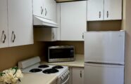 Apartment kitchen with over, stove-top, white cabinets and refrigerator.