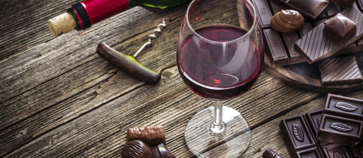 A glass of red wine and several pieces of chocolate on a wooden table.