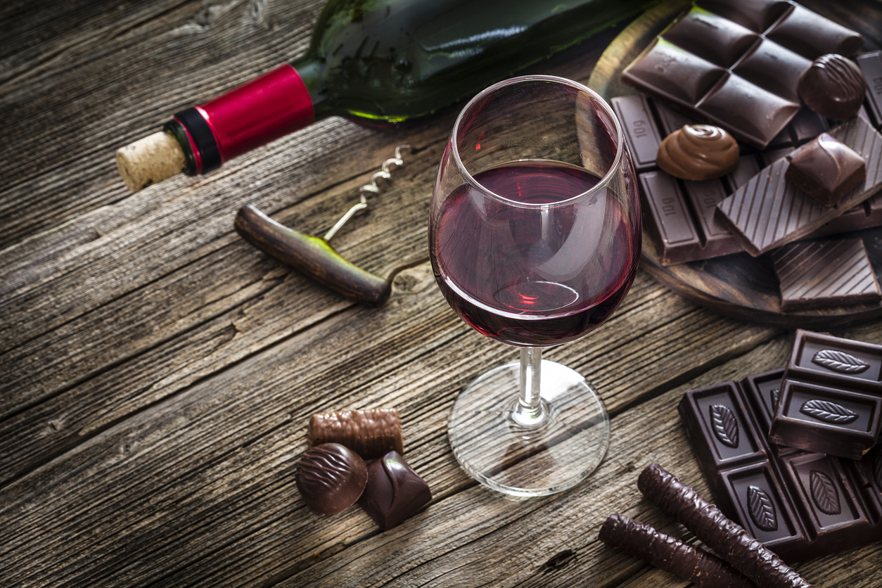 A glass of red wine and several pieces of chocolate on a wooden table.