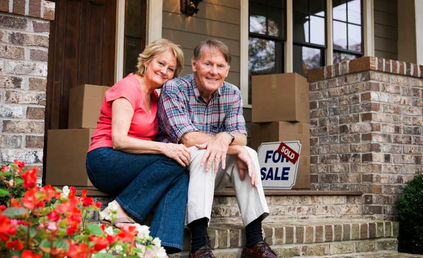 Happy older couple sitting on the front porch of home they have sold.