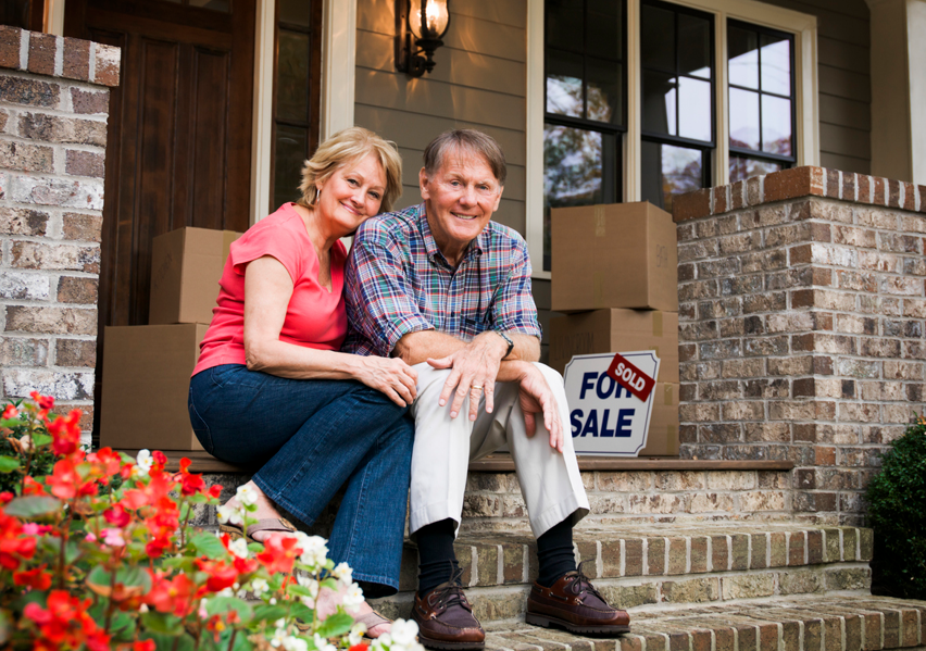 Happy older couple sitting on the front porch of home they have sold.