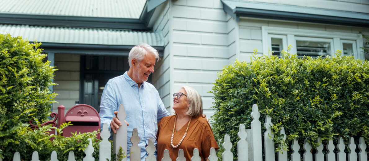 Smiling older couple standing in front of their home.